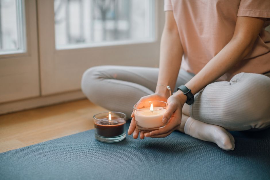 A person sits cross-legged holding a lit candle, promoting relaxation and meditation.
