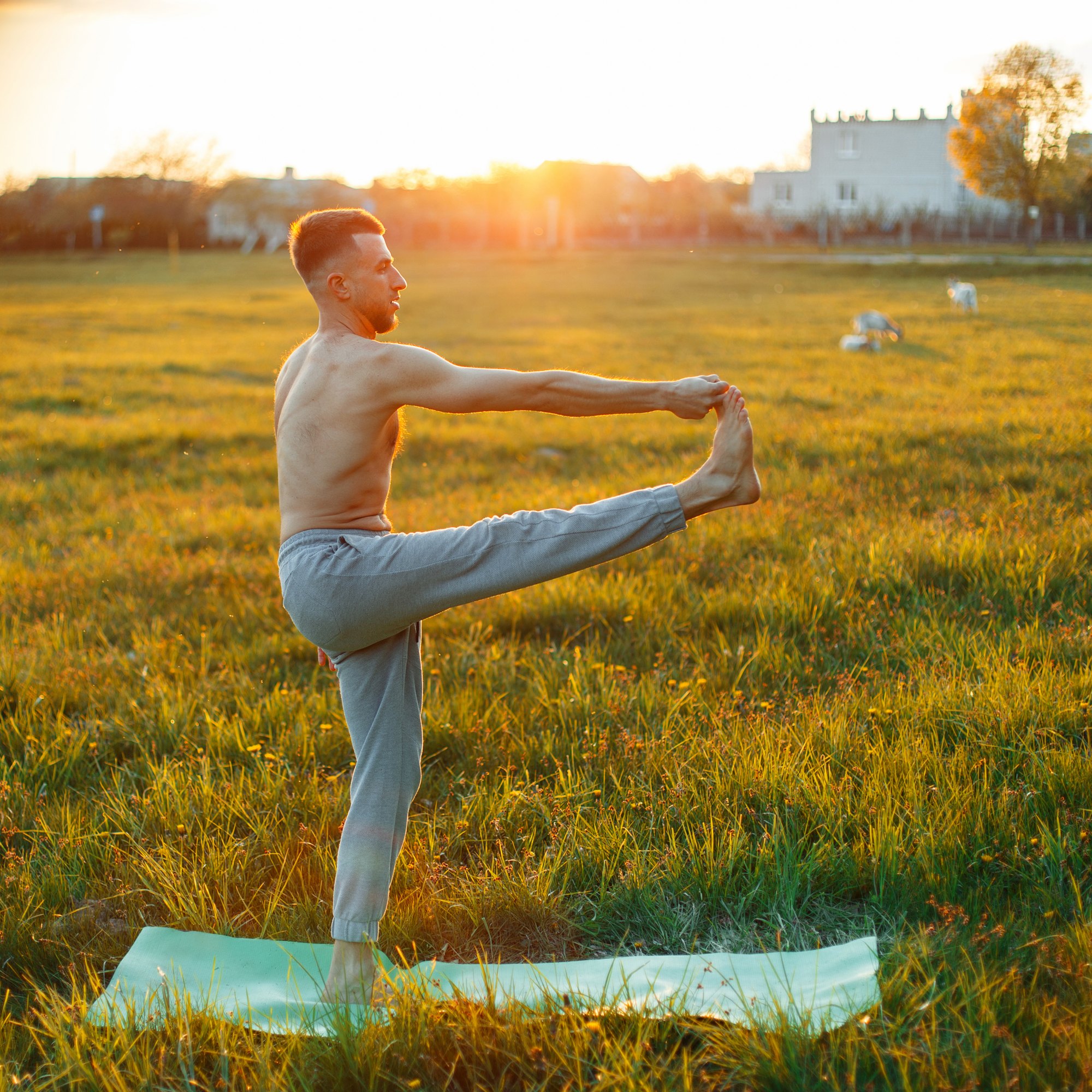 Man in extended hand-to-big-toe pose in a meadow at sunset