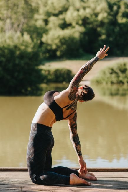Side view of anonymous barefoot female in sportswear standing on knees while stretching back on pier against pond