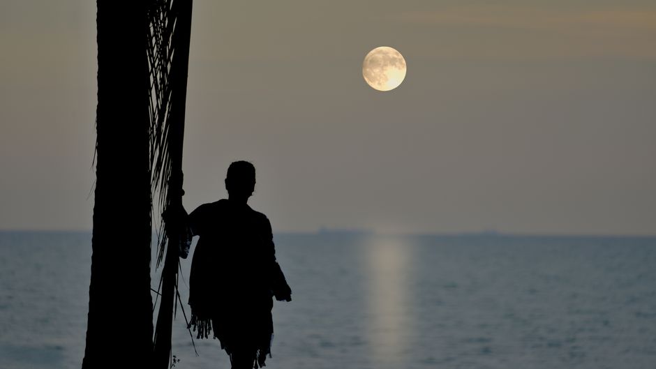 Silhouette of a person by the sea with a full moon in Port Dickson, Malaysia.