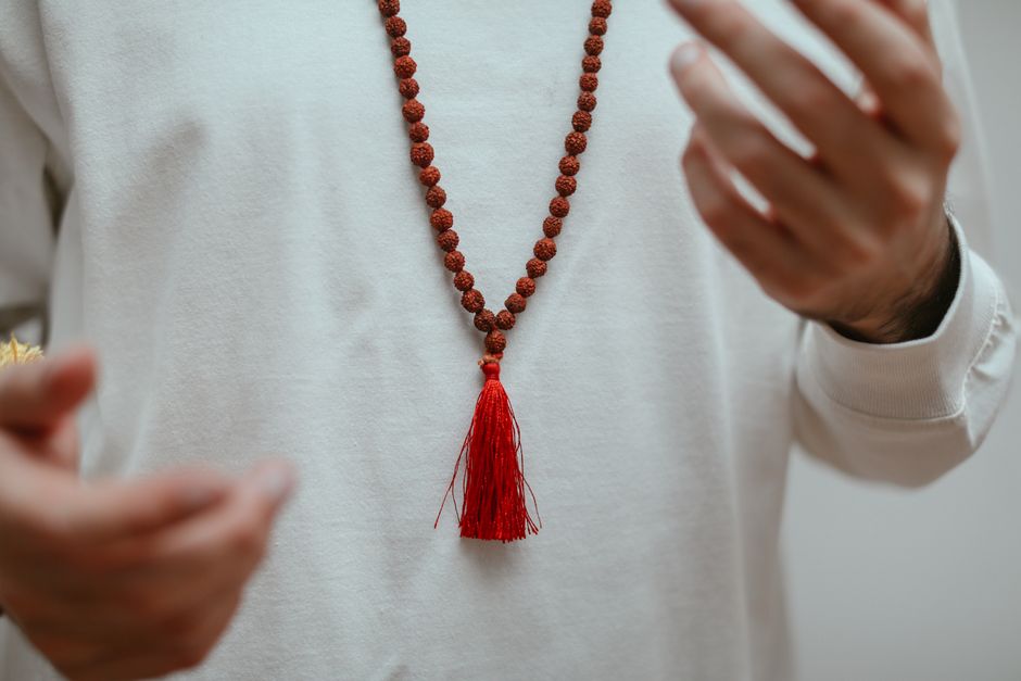 A detailed focus on hands showcasing a rudraksha mala necklace with red tassel.