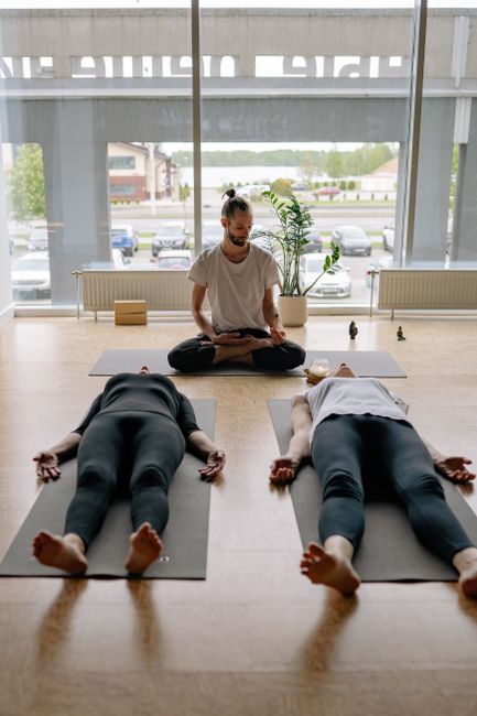 Instructor guides meditation for adults in yoga class with relaxation pose indoors.