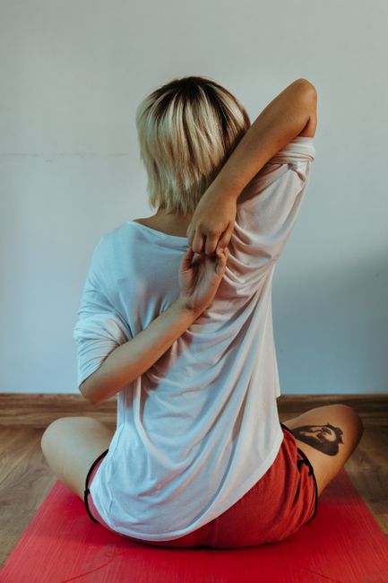Back view of female doing Cow face asana on red rubber mat on floor in room