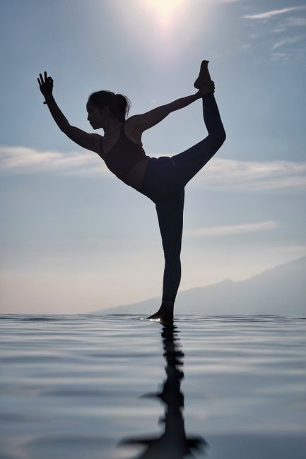 A woman performs a yoga pose on water at sunrise, creating a serene silhouette.