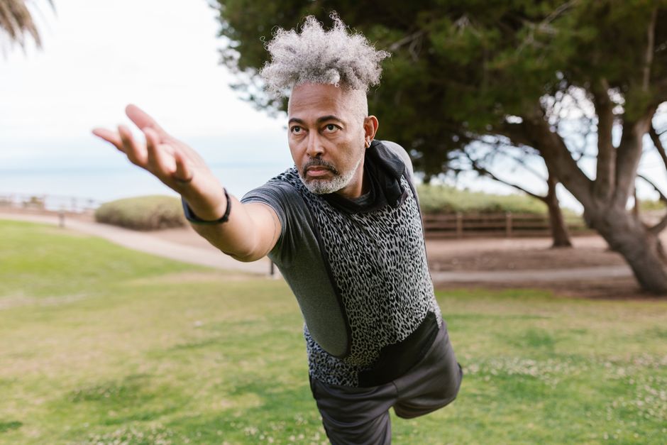 Middle-aged man in yoga pose on grassy field, emphasizing concentration and fitness.
