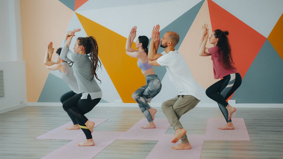 Five adults practicing yoga in a stylish studio with geometric wall design.