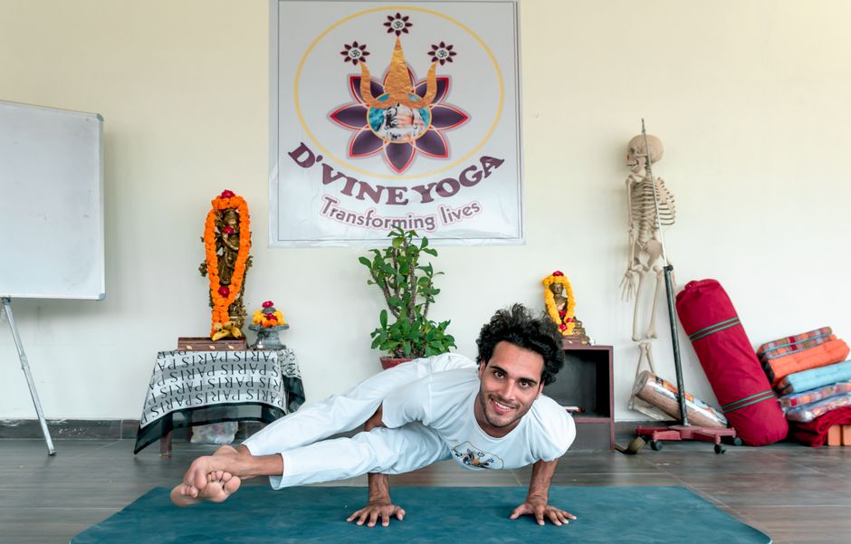 Man practicing eight angle yoga pose with a smile in a serene studio setting.