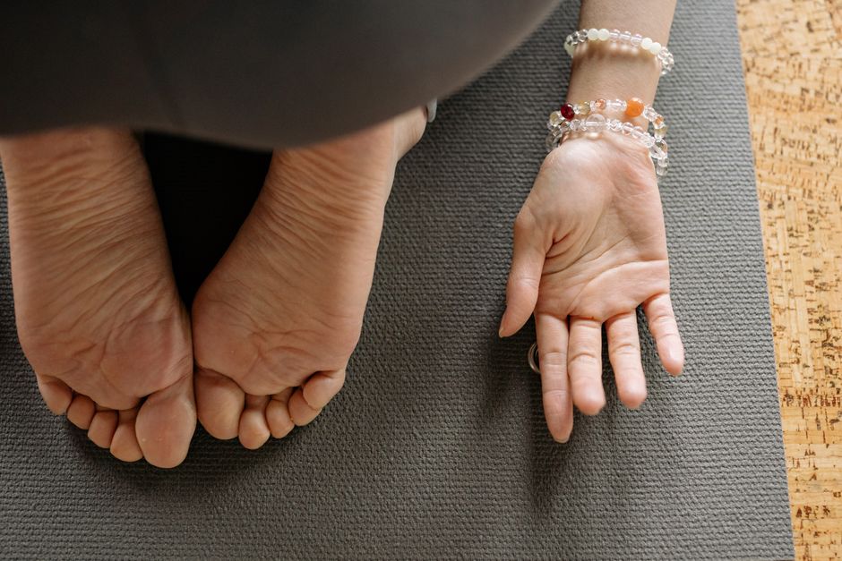 Feet and hand of a woman on yoga mat, showing bracelets and jewelry during exercise.