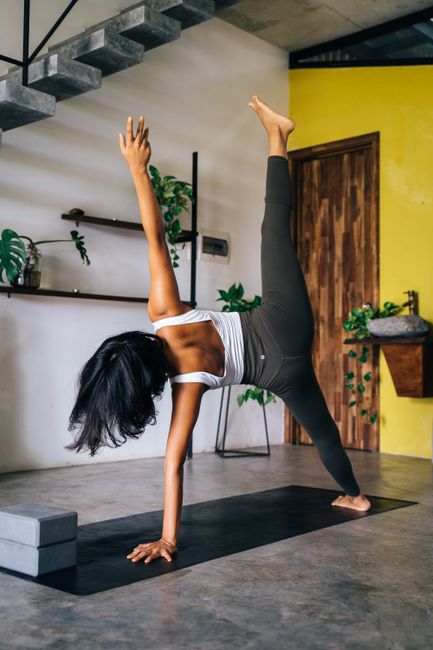Asian woman performing a yoga pose indoors, showcasing balance and strength.