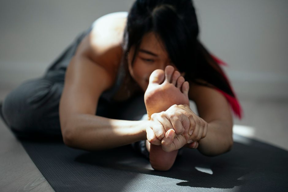 Crop young flexible Asian female bending forward while practicing Head to Knee I asana on mat during yoga session