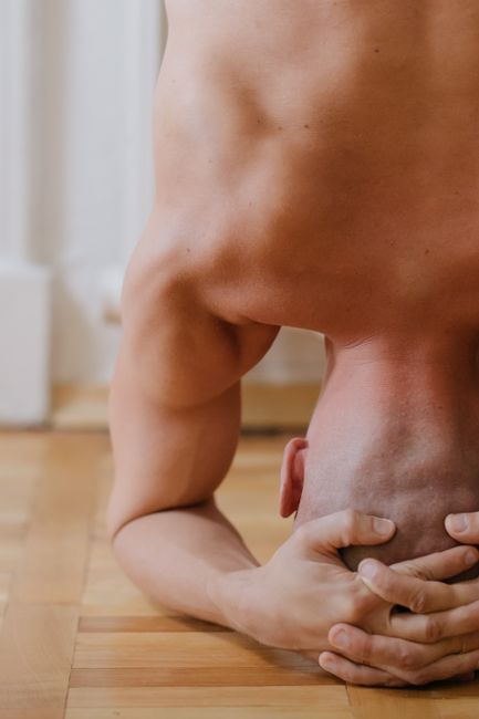 Bald man performing a headstand indoors on a wooden floor, showcasing strength and balance.
