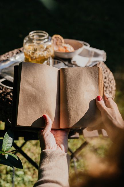 Hands holding an open book in a sunny garden with a tea set.