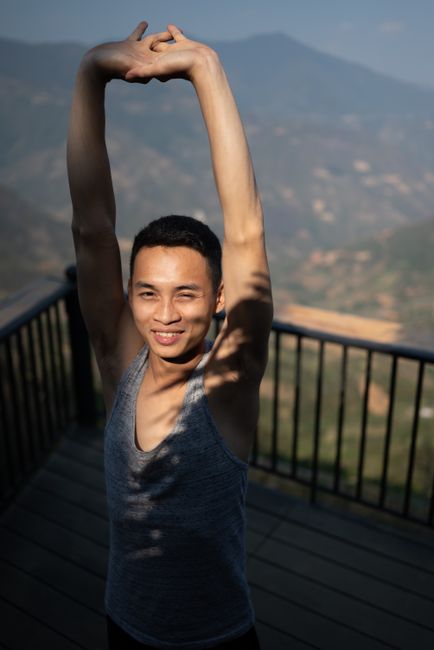 Smiling man stretching on a scenic outdoor deck with mountains in the background.