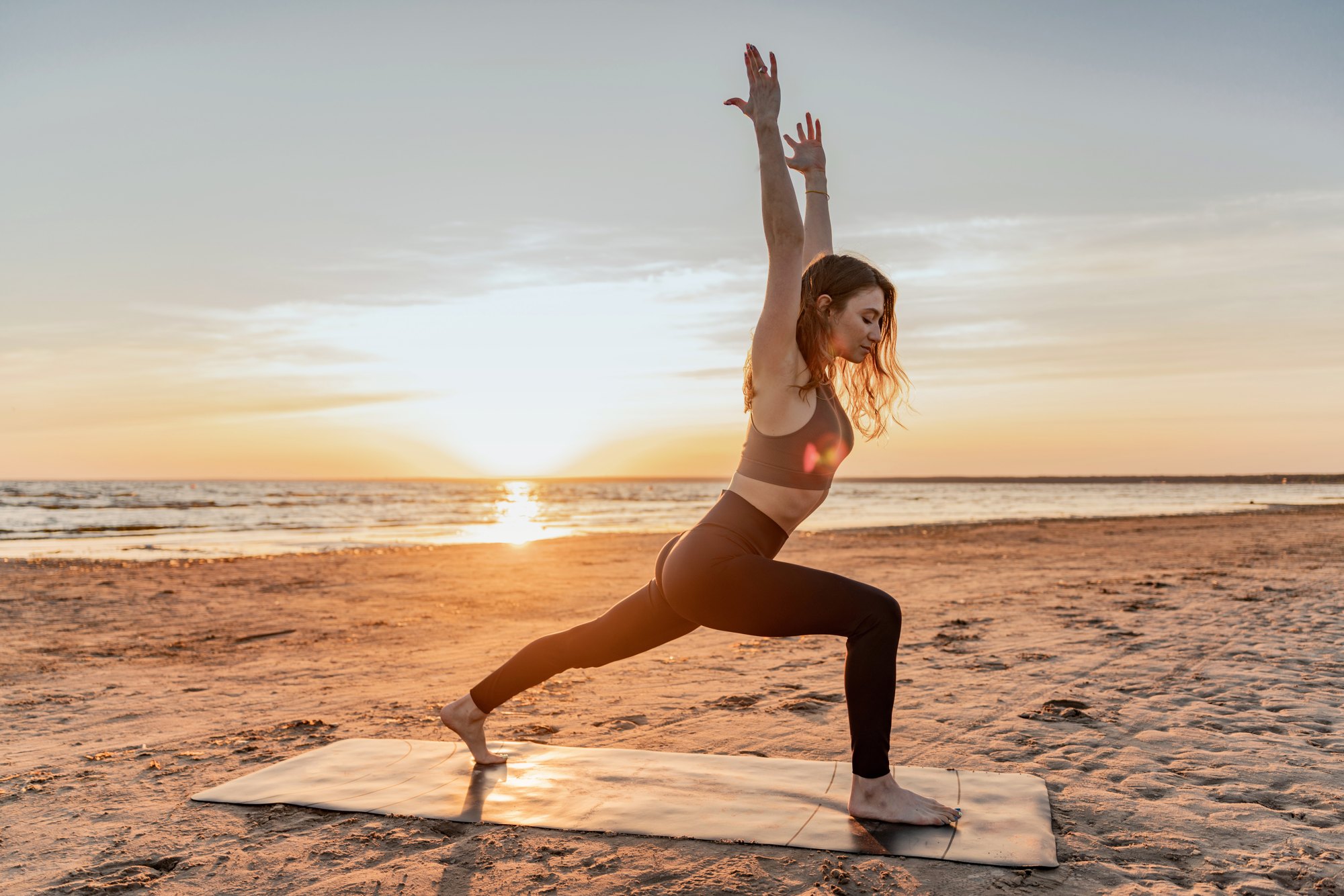 Woman in a warrior pose on a beach at sunrise