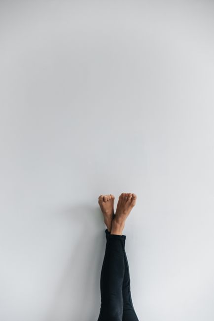 Minimalist image showing feet and legs in black leggings against a blank white wall.