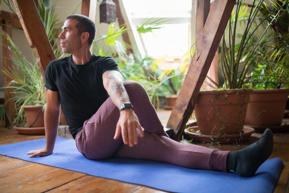 A man wearing activewear practices yoga on a mat indoors amid plants. Calm and focused.