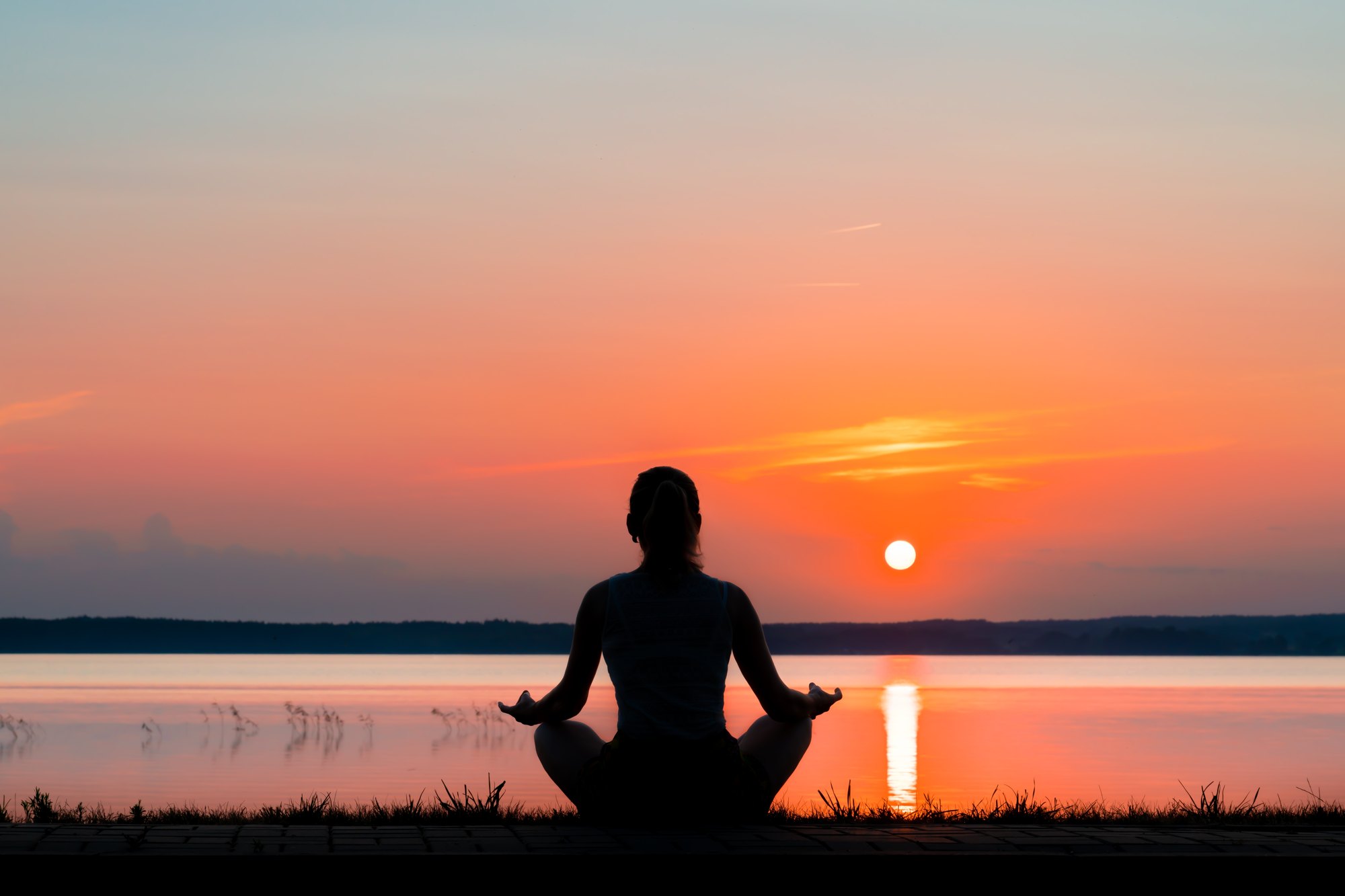 Silhouette meditating by a lake at sunset