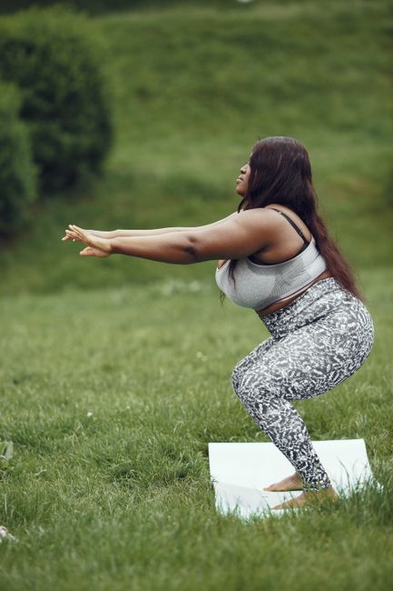 Curvy woman practicing yoga on a mat in a green park setting, embodying healthy lifestyle.