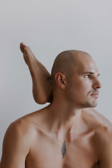 Artistic portrait featuring a bald man and a foot raised behind him on a white background.