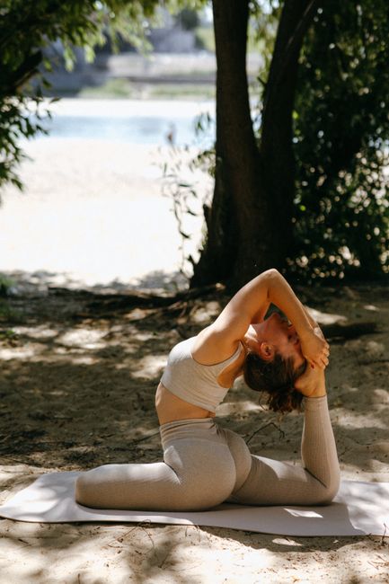 Woman practicing yoga one-legged pigeon pose outdoors in sunny forest.