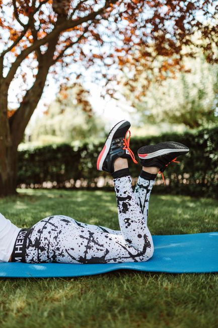 Woman lying on blue yoga mat outdoors, wearing activewear and sneakers.