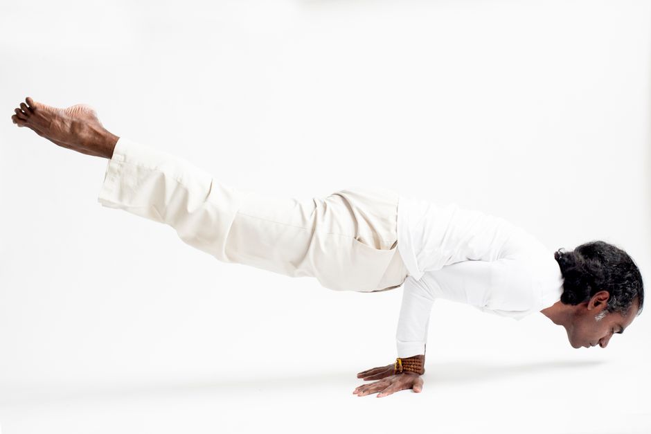 A man performs a challenging yoga pose wearing white clothes on a clean white background.