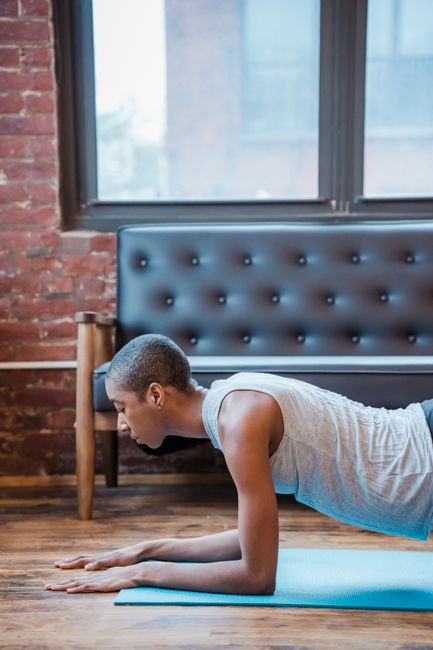 Side view of focused African American female in activewear practicing Phalakasana posture on mat during intense yoga training at home