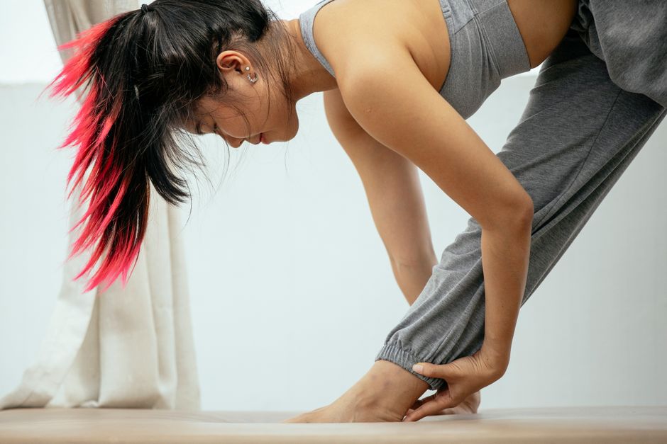 Side view ground level of peaceful ethnic female with pink hair practicing yoga in Parsvottanasana while stretching legs on terrace