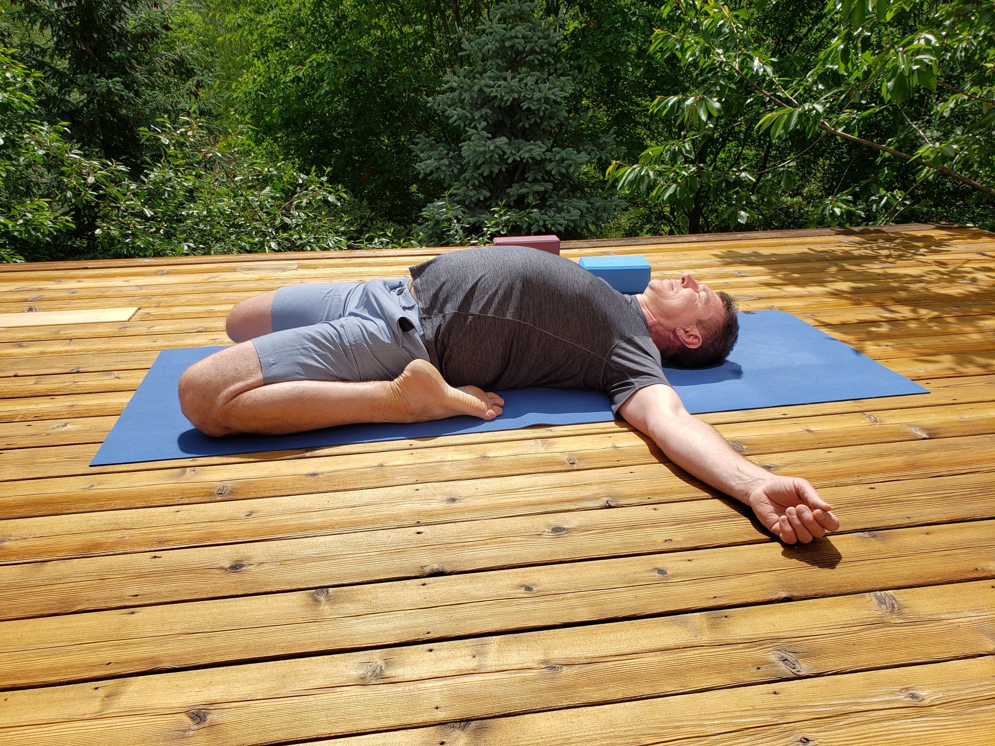 Man in reclining bound angle pose on a wooden deck