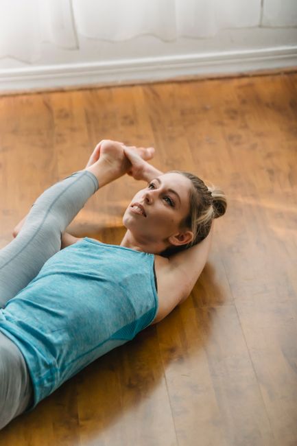 From above of sportive barefoot female doing Extended supine hand to toe posture while lying on floor during yoga workout