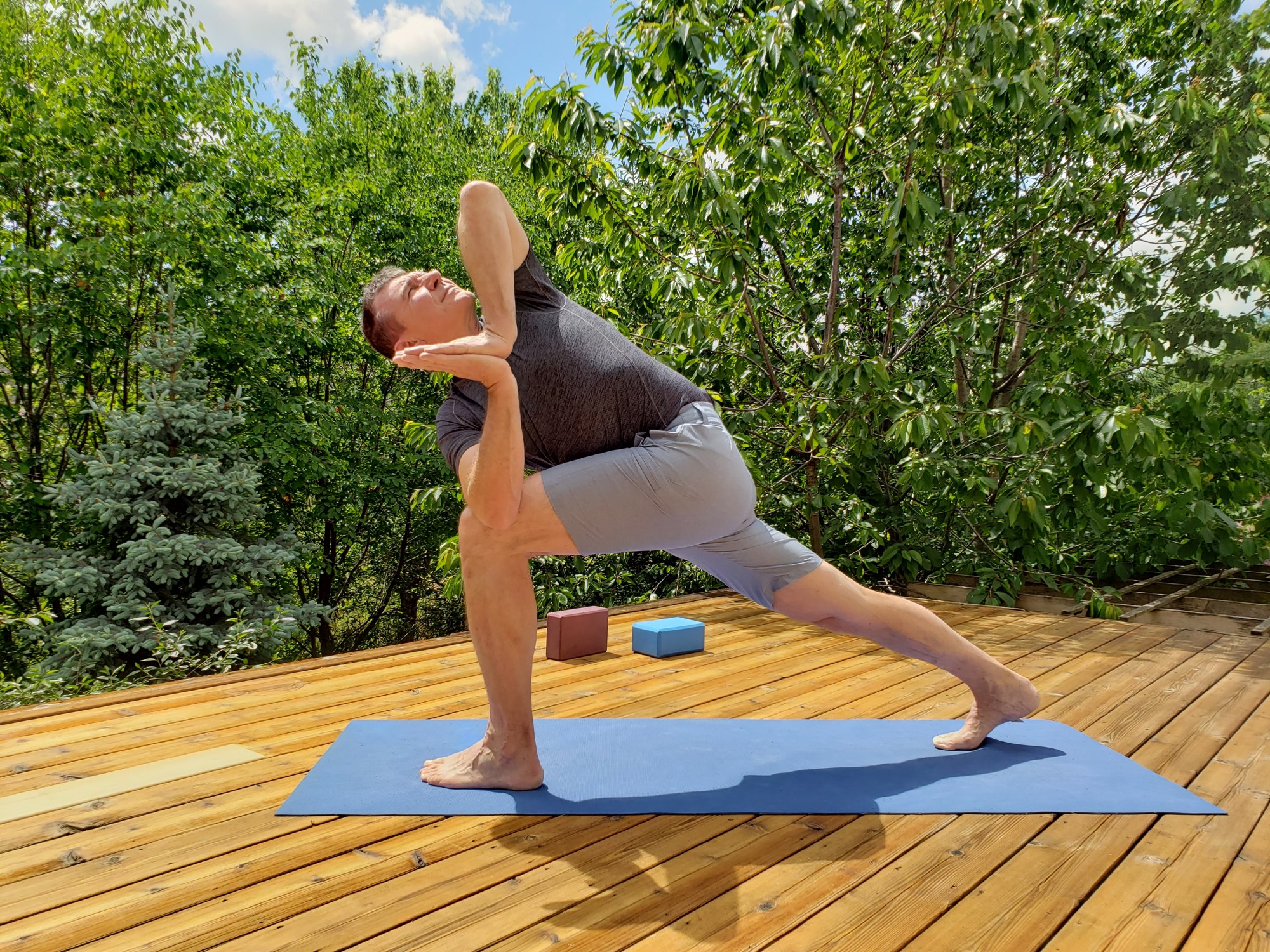 Revolved side angle with prayer hands on a garden deck