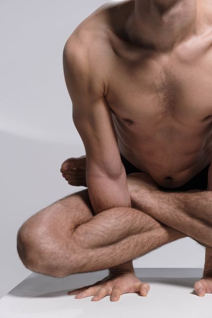 A shirtless man demonstrates a complex yoga pose, showcasing flexibility and muscular strength.