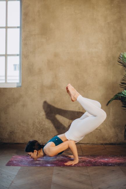 Woman performing scorpion pose on a yoga mat in a serene, indoor studio setting.