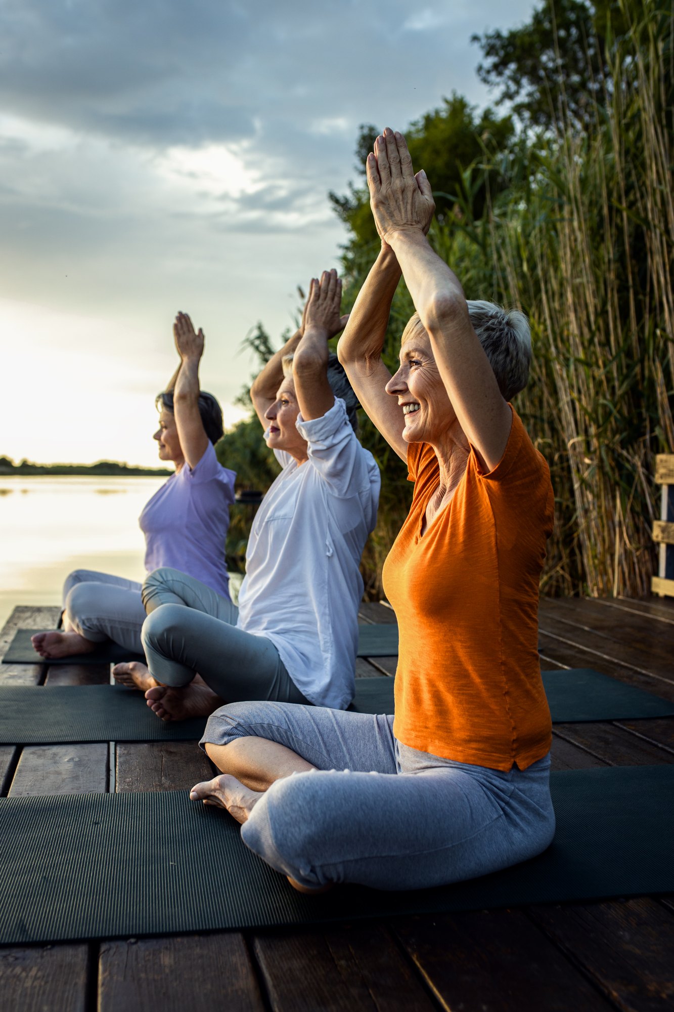 Seniors raising their arms on a lakeside deck