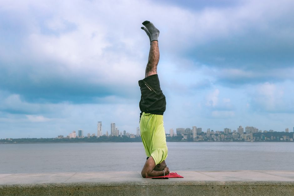 A person performs a yoga headstand on Marine Drive, Mumbai with the city skyline in the background.
