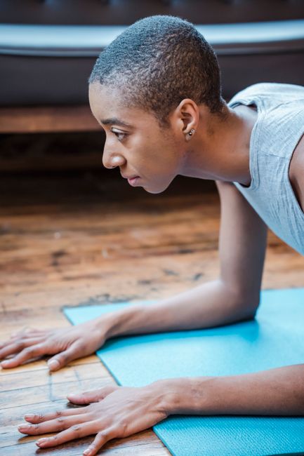 Side view of sportive African American female with short hair practicing Phalakasana posture on mat during intense yoga workout