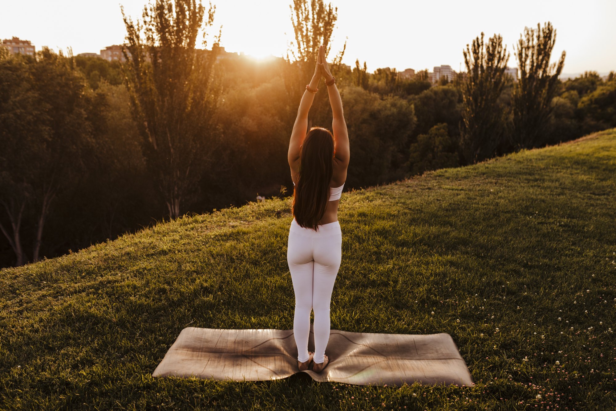 Woman reaching up at the start of Sun Salutation A on a hillside