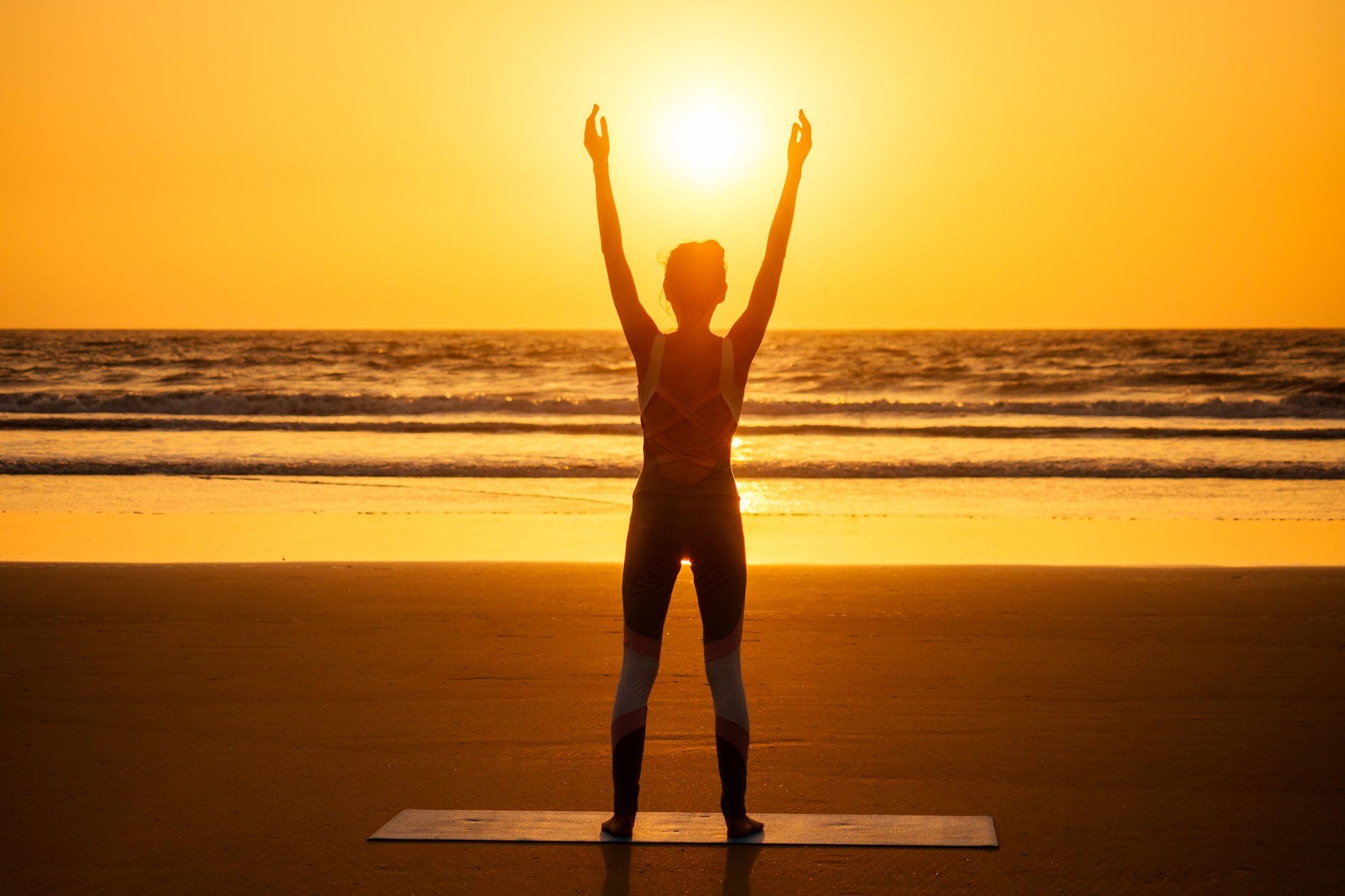 Woman raising her arms to the sun on a beach at sunset