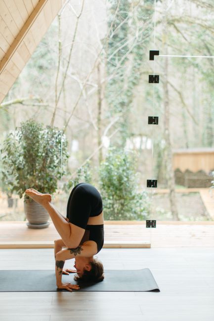 Adult woman in black activewear performing a headstand yoga pose indoors on a mat.