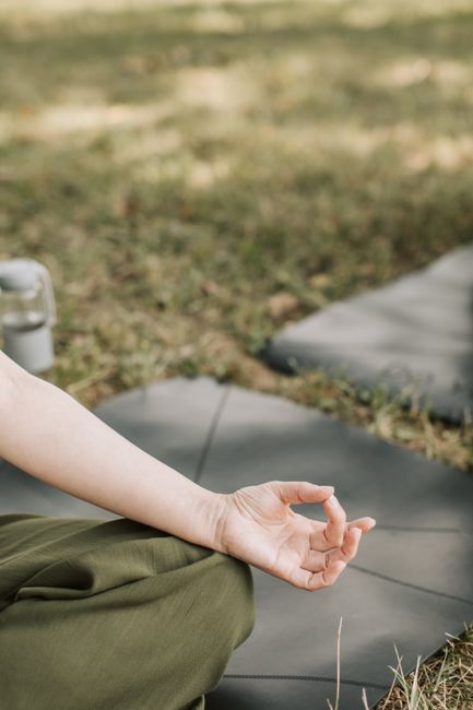 A peaceful outdoor meditation with focus on hand positioning in a grassy field.
