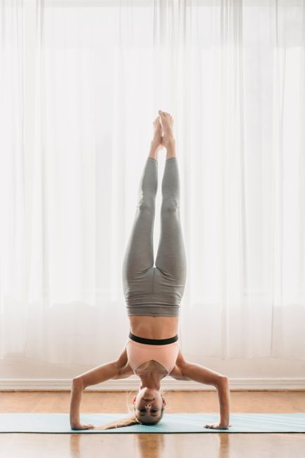 Full body of calm barefooted young female yogi performing Salamba Sirsasana B pose during Ashtanga Vinyasa yoga training in studio in sunny morning