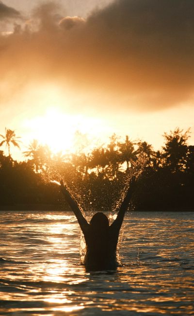Silhouette of a person in water with outstretched arms during a vibrant sunset.