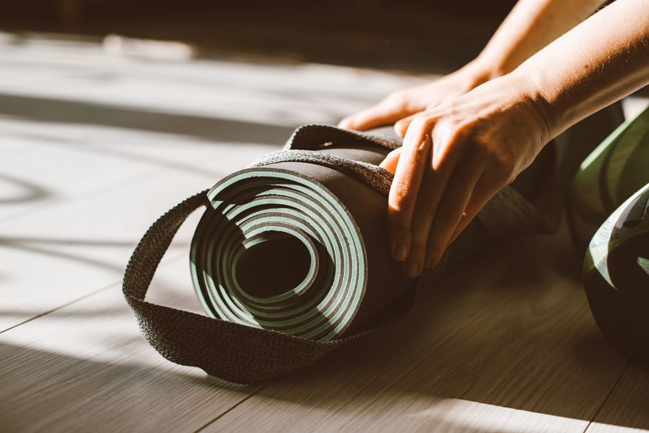 Close-up of hands rolling up a yoga mat on a sunny hardwood floor indoor setting.