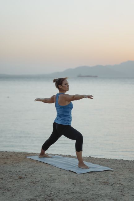 Woman performing Warrior 2 pose on the beach during twilight, combining fitness and tranquility.