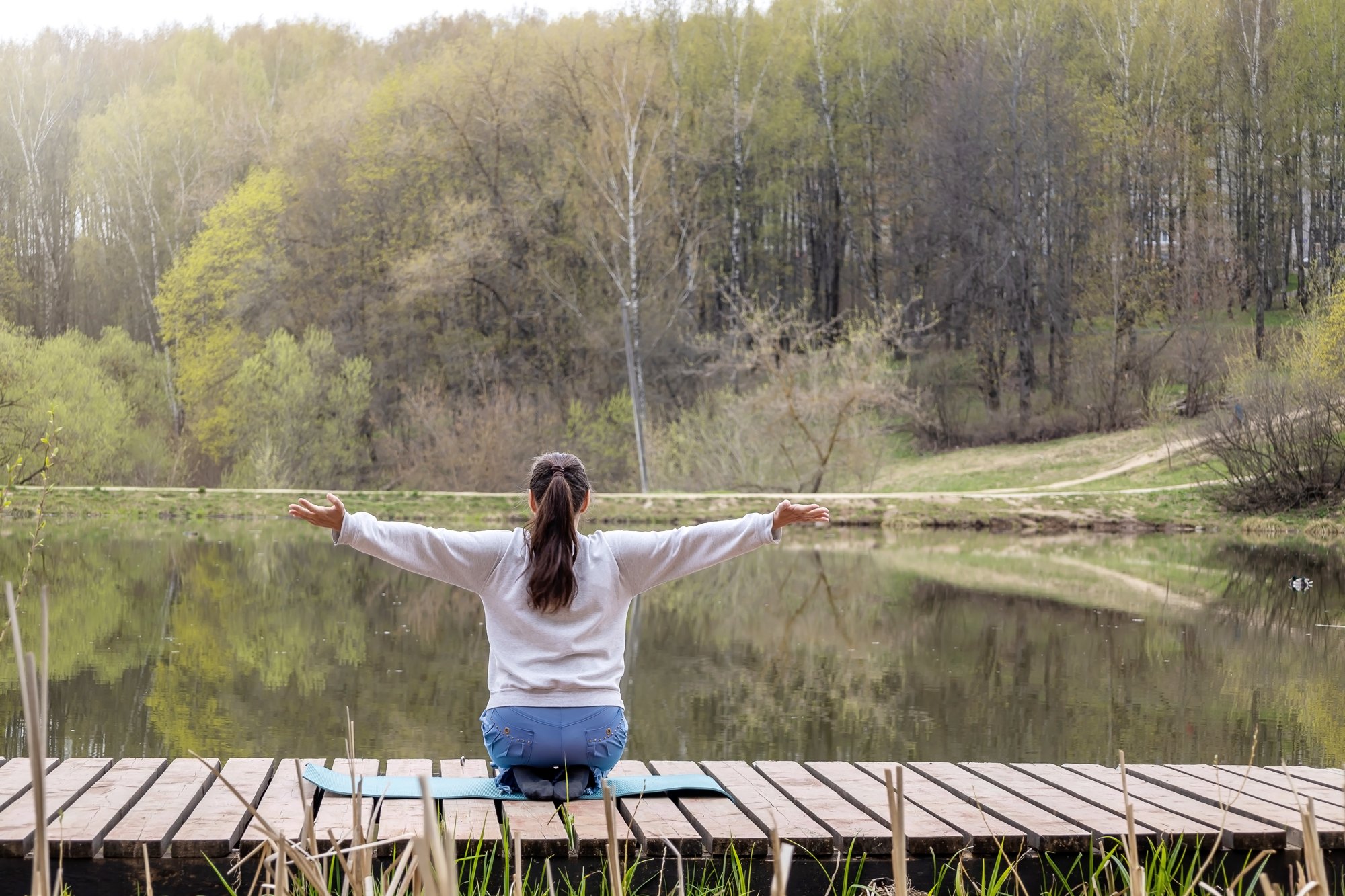 Woman sitting on a lakeside dock with arms open