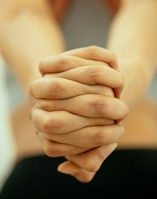 Crop hands of unrecognizable female showing clasped hands while stretching body in light room on blurred background