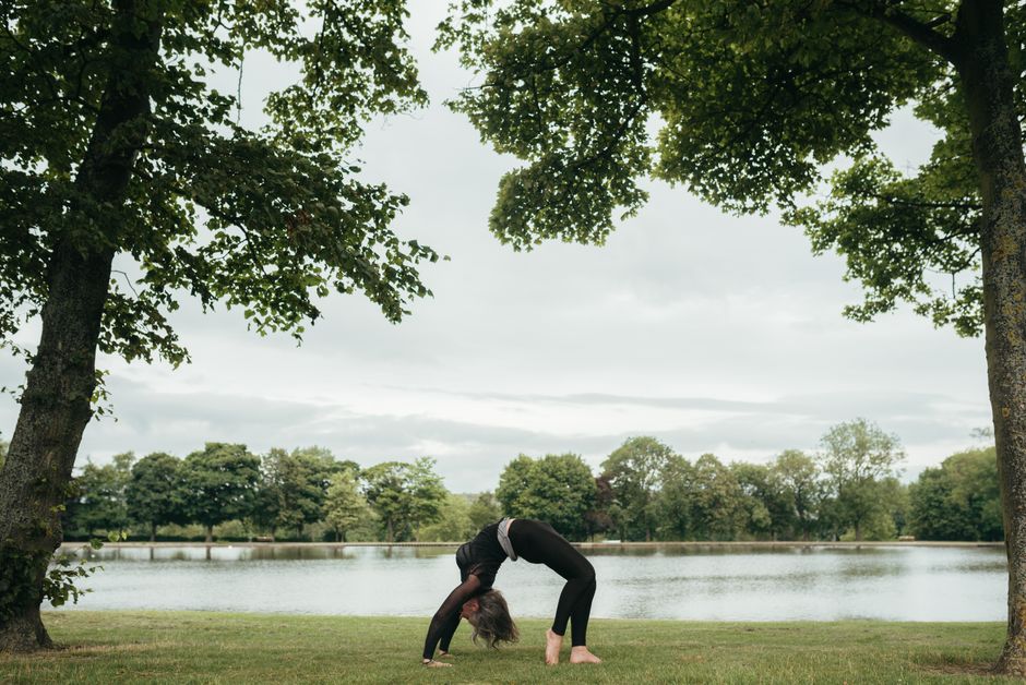 Side view of anonymous slim lady in sportswear standing in Urdhva Dhanurasana pose while practicing yoga on river shore