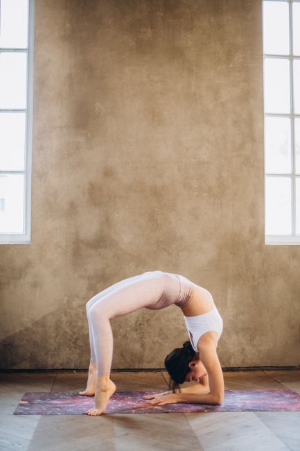 Woman performs wheel pose on yoga mat in bright indoor setting, showcasing strength and flexibility.