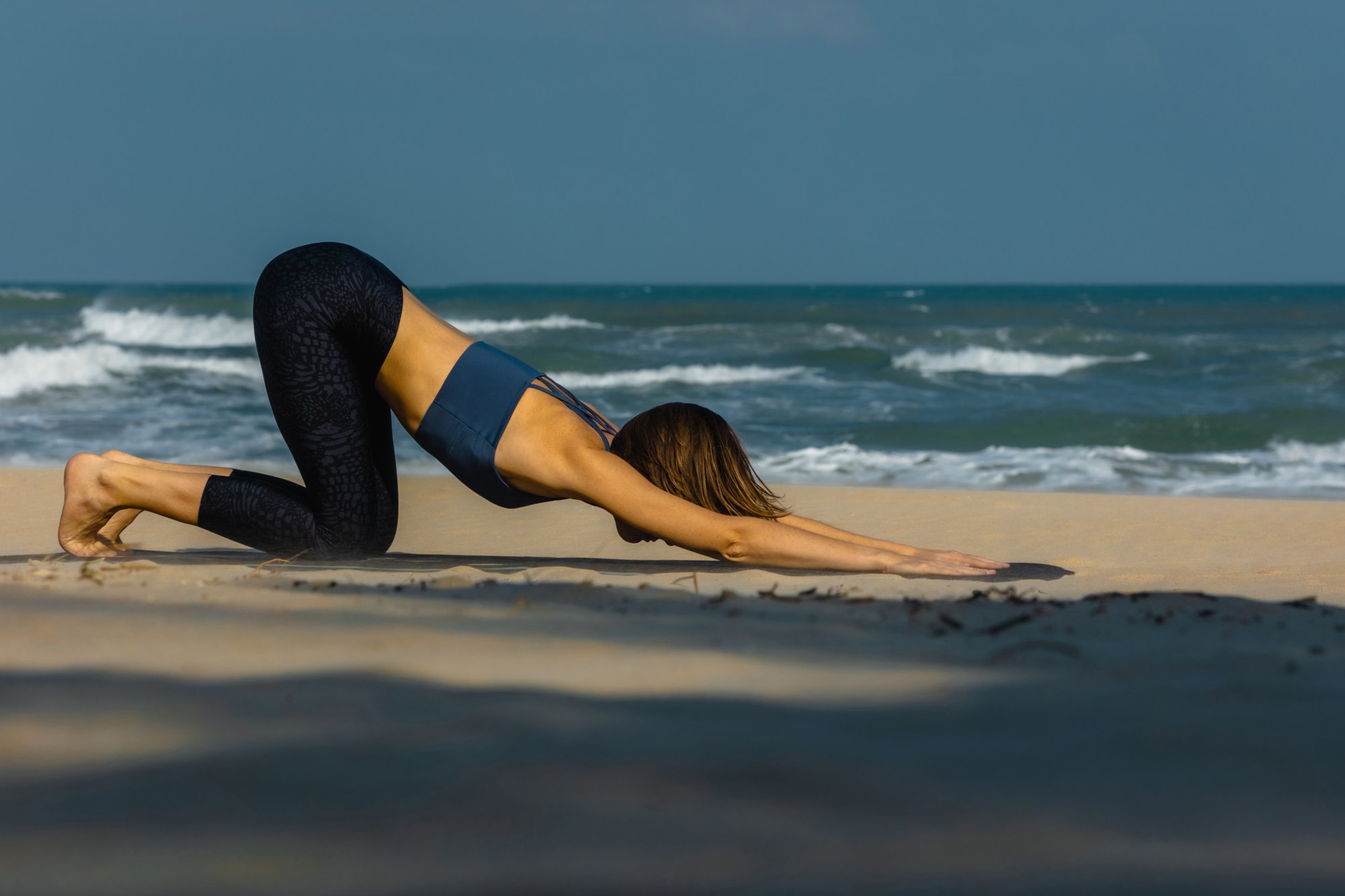 Melting heart pose on a beach by the waves