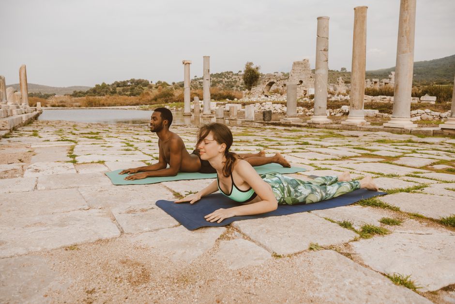 Sphinx (Yin): Two people practicing yoga on mats near ancient ruins, embracing a healthy lifestyle.